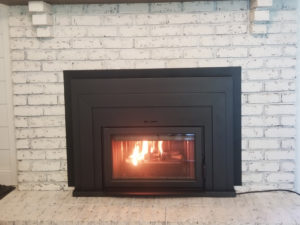A fireplace with a black mantle and white brick offering chimney services.