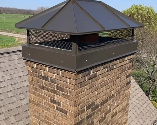 A brick chimney on a shingled roof features a black metal chimney cap with mesh sides and a sloped top, set against trees and open fields—a perfect example of expert Chimney services for safety and style. Chimney & Dryer Vent Services, LLC A brick chimney on a shingled roof features a black metal chimney cap with mesh sides and a sloped top, set against trees and open fields—a perfect example of expert Chimney services for safety and style. Chimney & Dryer Vent Services, LLC